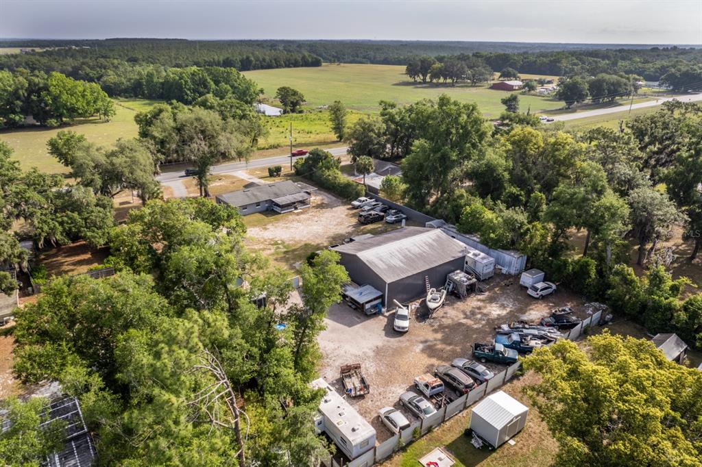 An aerial view shows a house, a large metal workshop, and vehicles on a rural lot — 20024 STATE ROAD 44, EUSTIS, FL
