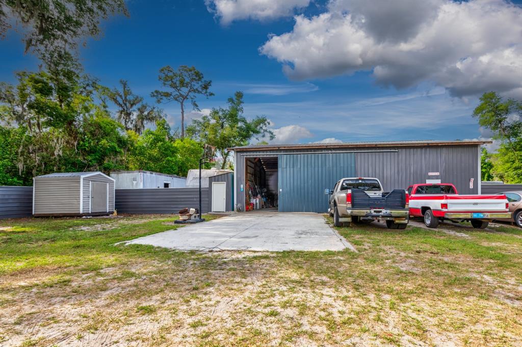 A metal workshop building with a concrete driveway, two parked trucks, and a storage shed — 20024 STATE ROAD 44, EUSTIS, FL