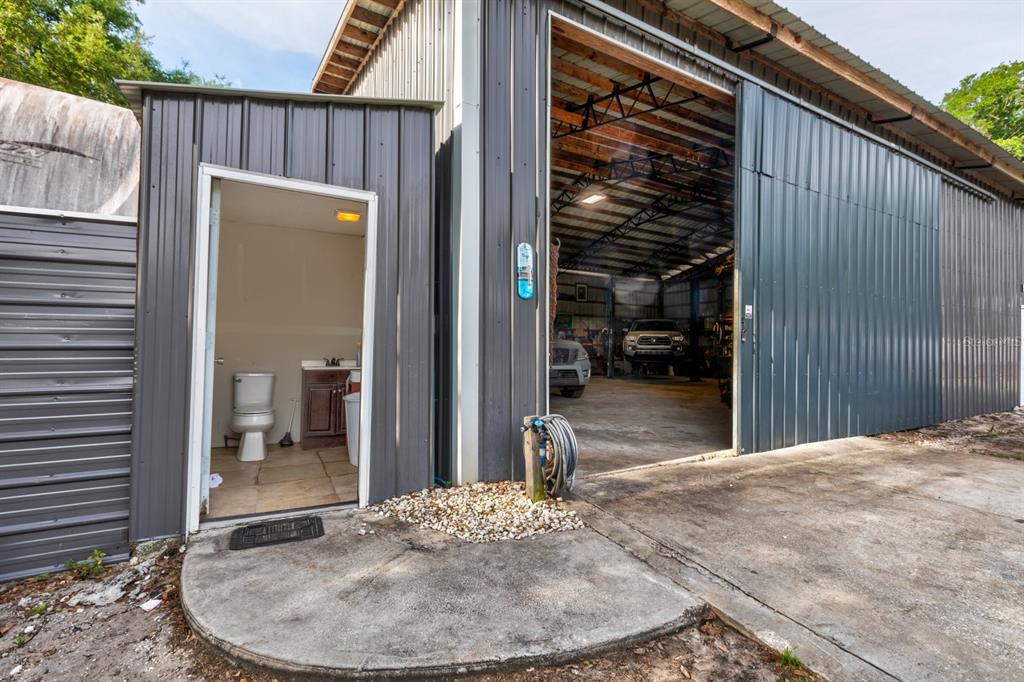 A small outdoor bathroom with a toilet and vanity sits beside a large metal workshop — 20024 STATE ROAD 44, EUSTIS, FL