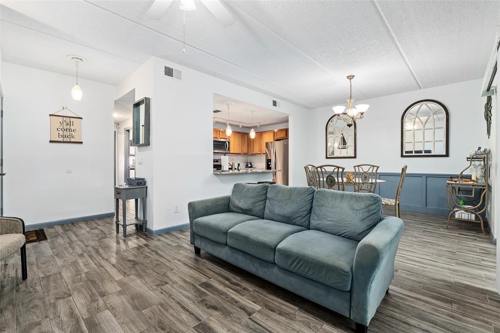 A living room with a blue sofa, wood-look flooring, and an open view into the kitchen — 35 NAVARRA COURT UNIT 35, ST AUGUSTINE, FL