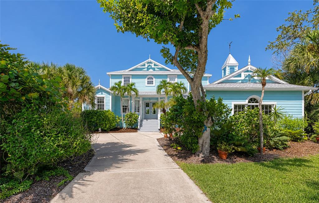 A light blue two-story house with a concrete driveway and lush landscaping under a clear sky — 5334 CALLE FLORIDA, SARASOTA, FL