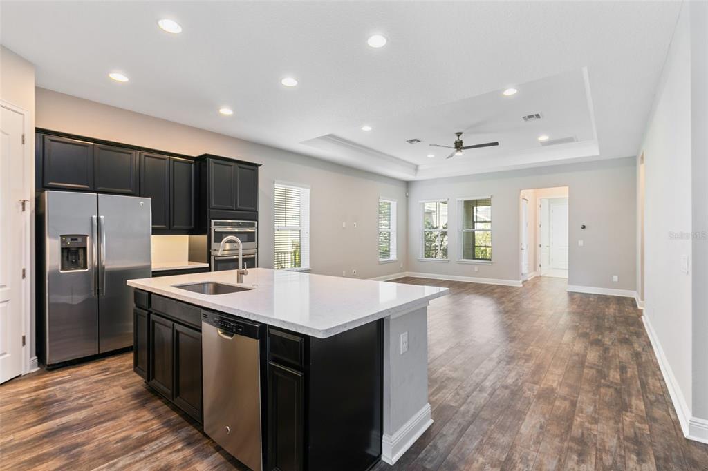 A kitchen with dark cabinets and a white island overlooks an open-concept living area — 9211 NEHER STREET, ORLANDO, FL