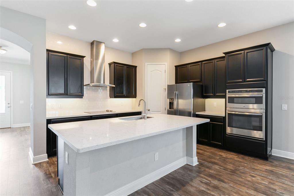 A modern kitchen features dark cabinetry, a white quartz island, and stainless steel appliances — 9211 NEHER STREET, ORLANDO, FL