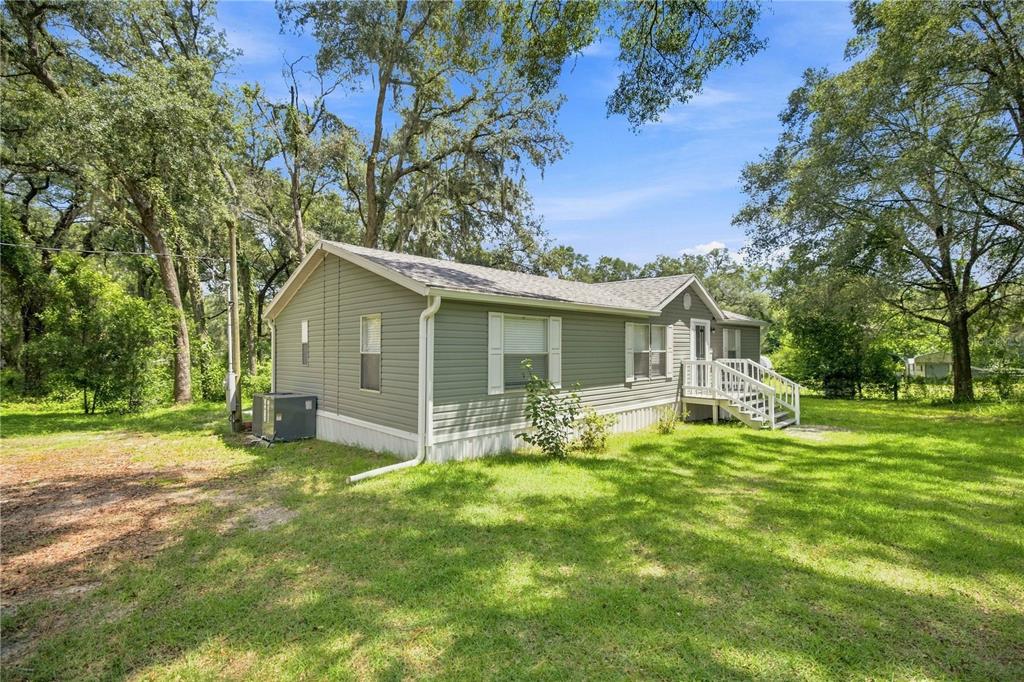 A light green manufactured home sits on a grassy lot surrounded by large oak trees — 2545 SE 178TH STREET, SUMMERFIELD, FL