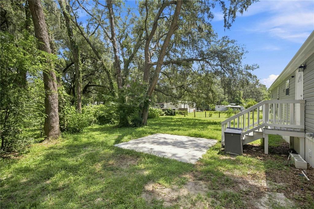 A backyard features a small concrete patio, a wooden staircase, and large trees — 2545 SE 178TH STREET, SUMMERFIELD, FL