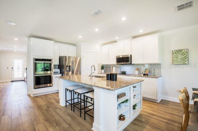 A modern kitchen features white cabinetry, granite countertops, a central island with seating, and stainless appliances — 3418 MONARCH WAY, GREEN COVE SPRINGS, FL