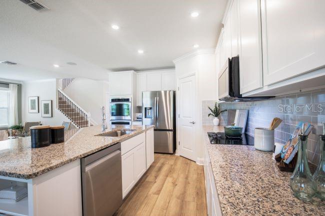 A kitchen features white cabinets, granite countertops, stainless steel appliances, and wood-look flooring — 3418 MONARCH WAY, GREEN COVE SPRINGS, FL