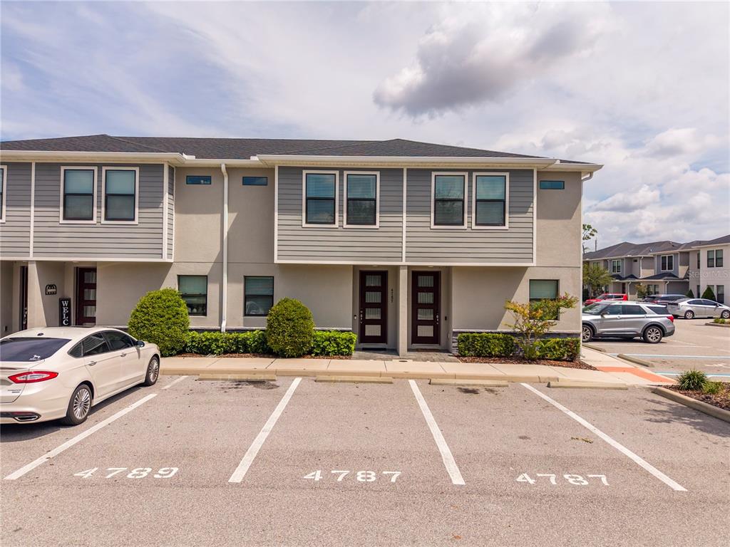 A two-story townhouse exterior features gray siding, stucco walls, and assigned parking spaces — 4787 TERRA ESMERALDA DRIVE, KISSIMMEE, FL