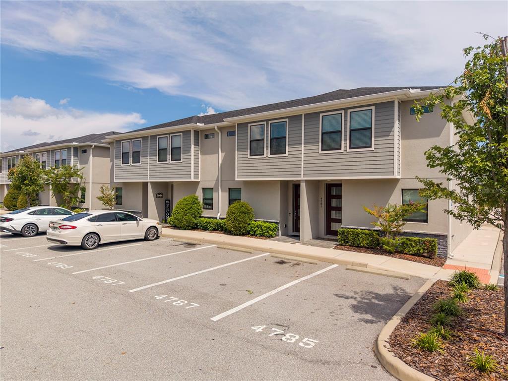 A two-story townhouse exterior with gray siding, tan stucco, and a paved parking lot — 4787 TERRA ESMERALDA DRIVE, KISSIMMEE, FL