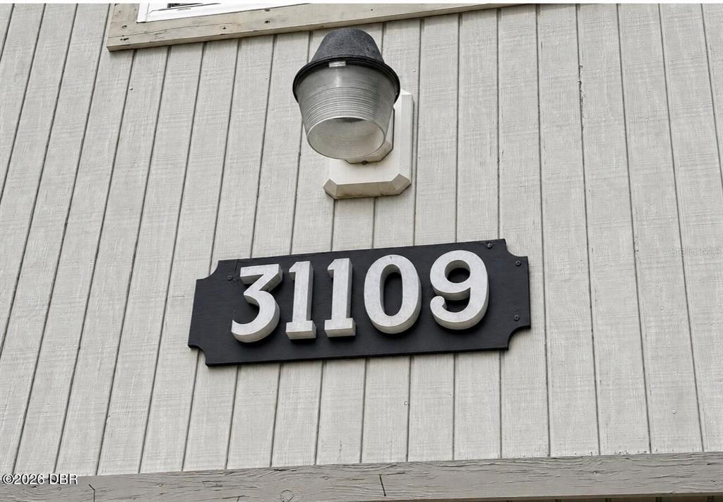 A black house number plaque with white digits is mounted on light-colored vertical wood siding — 31109 DEAL DRIVE, MOUNT PLYMOUTH, FL