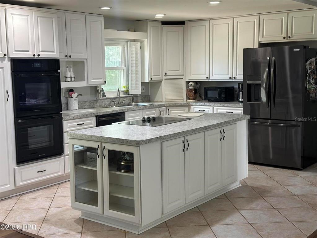 A kitchen features white cabinetry, a central island with glass-front cabinets, and stainless steel appliances — 31109 DEAL DRIVE, MOUNT PLYMOUTH, FL