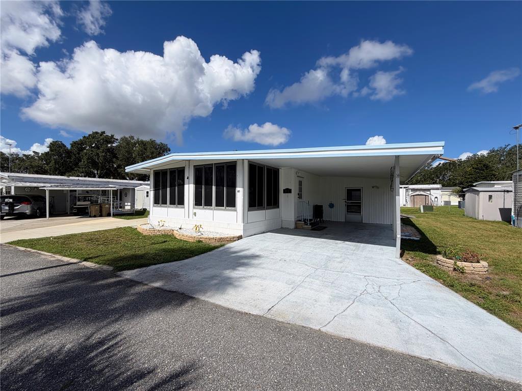 A single-story mobile home with a carport, screened-in porch, and concrete driveway — 751 TRACI DRIVE, LEESBURG, FL