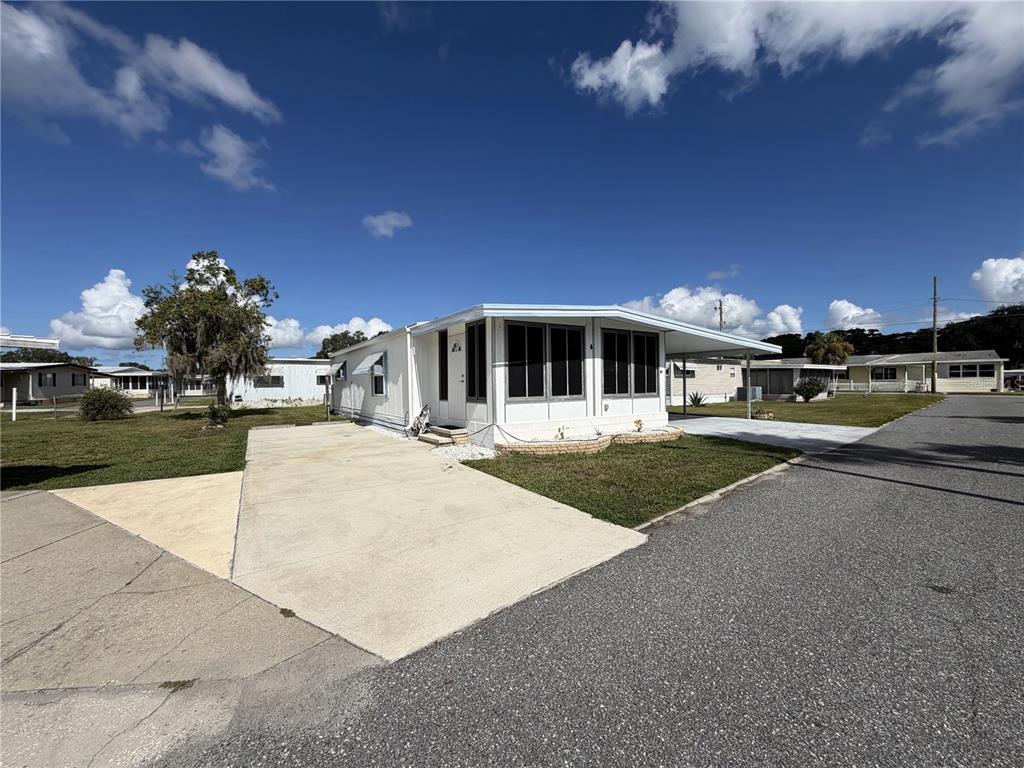 A white mobile home with a screened-in porch and a concrete driveway under a blue sky — 751 TRACI DRIVE, LEESBURG, FL
