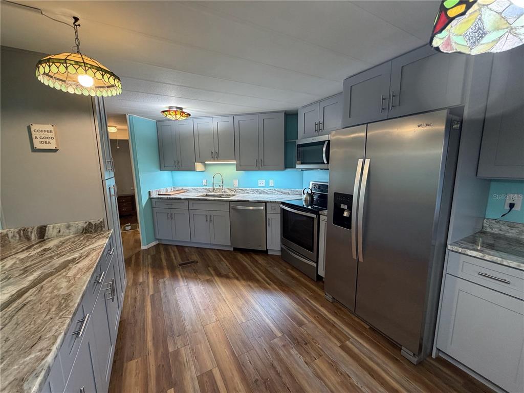 A kitchen features grey cabinets, stainless steel appliances, wood-look flooring, and a light blue backsplash — 751 TRACI DRIVE, LEESBURG, FL