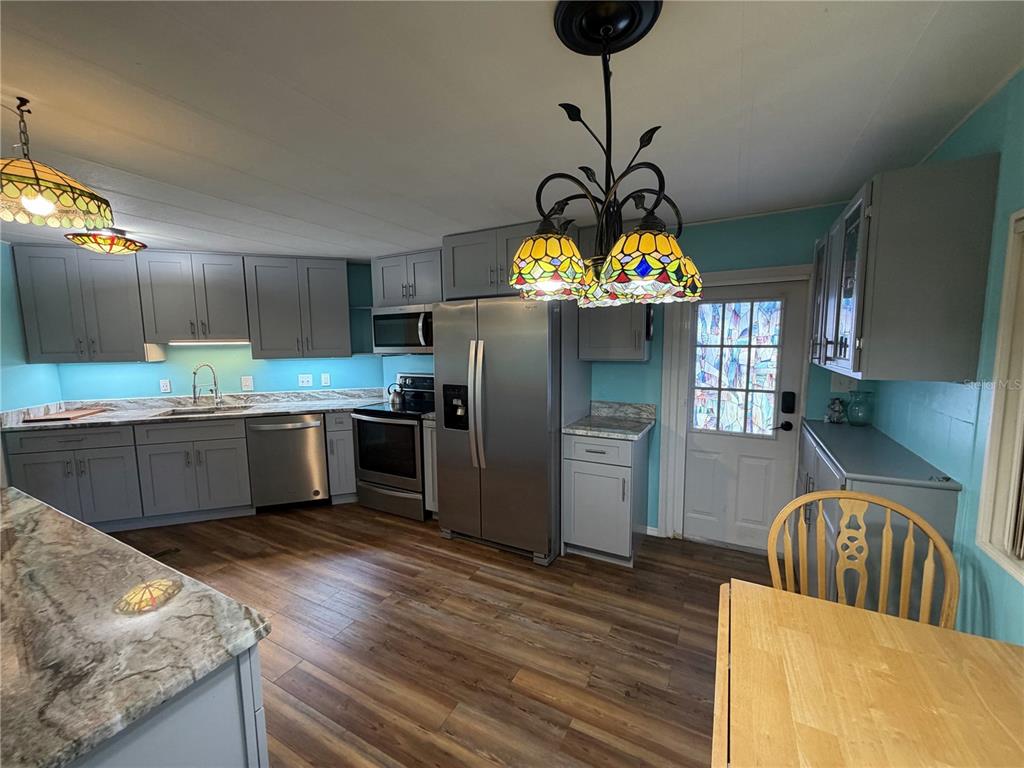 A kitchen features gray cabinets, stainless steel appliances, wood-look flooring, and bright teal walls — 751 TRACI DRIVE, LEESBURG, FL