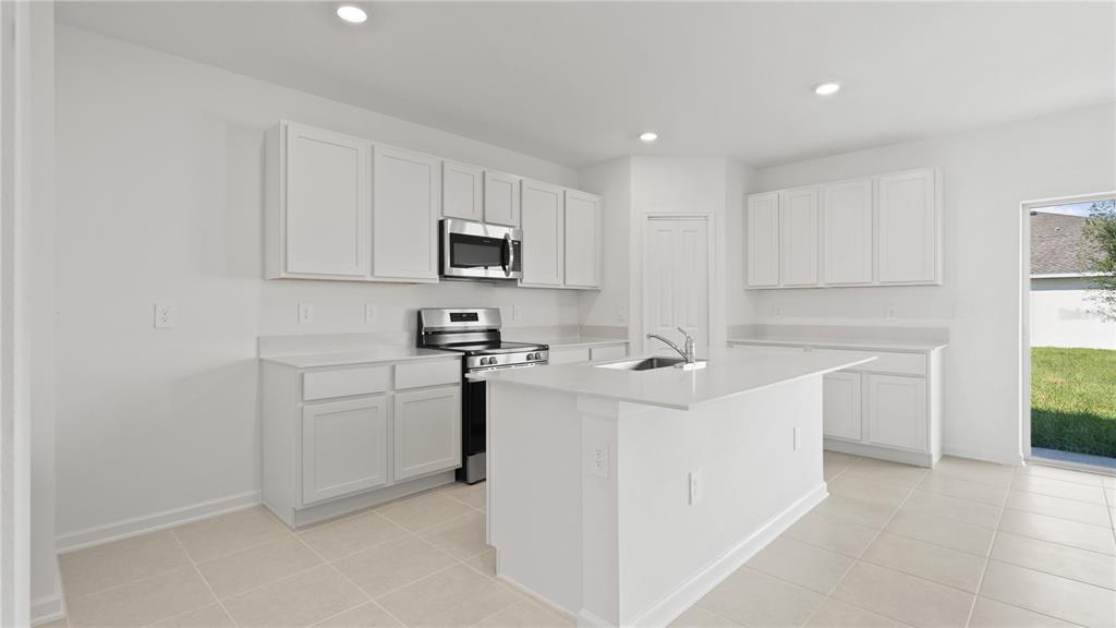 A bright kitchen features white cabinets, stainless steel appliances, a center island, and tile flooring — 6257 BOTTICELLA BOULEVARD, WINTER HAVEN, FL