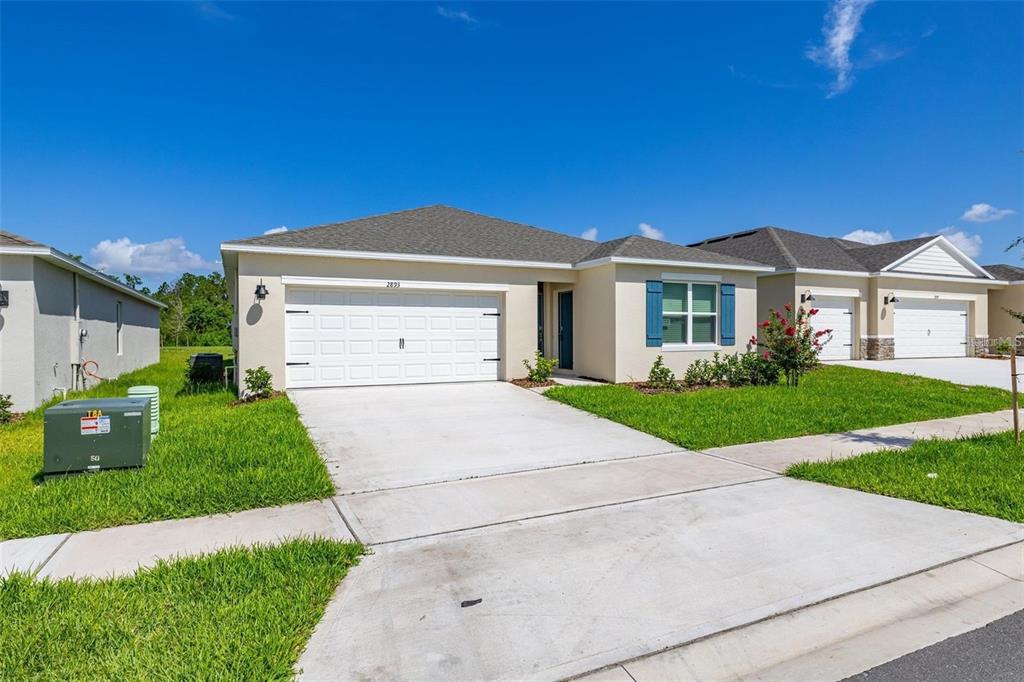 A single-story suburban house with a white garage, beige siding, and blue window shutters — 2893 HOUSE FINCH ROAD UNIT A, HARMONY, FL