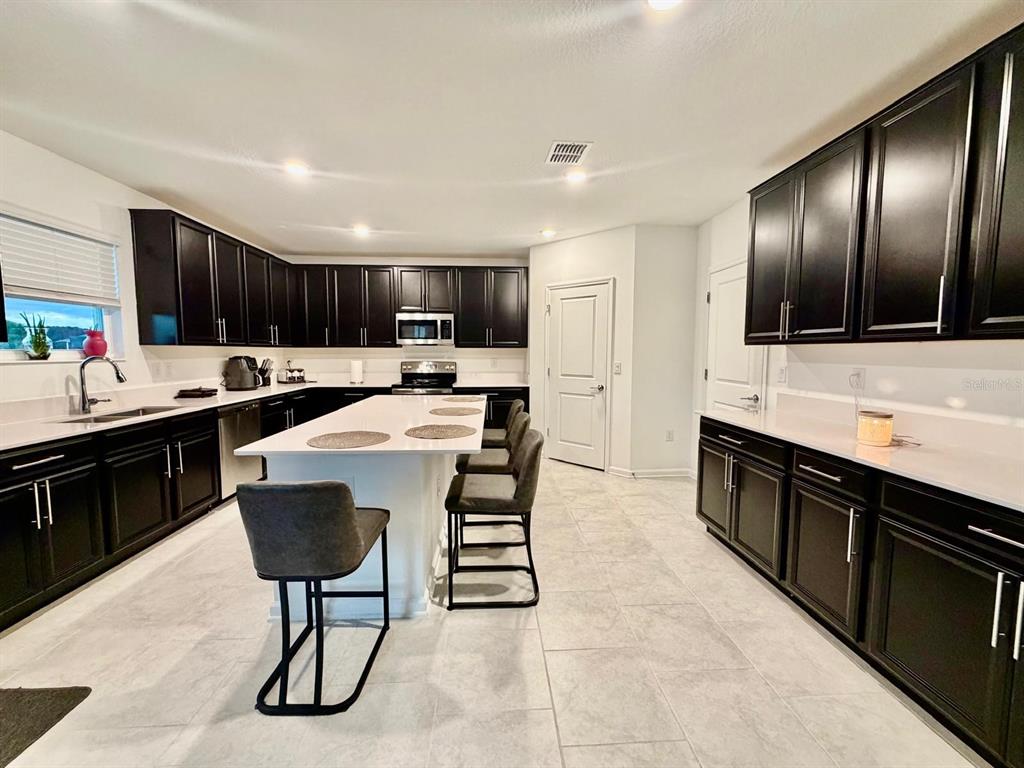 A kitchen features dark cabinetry, white countertops, a central island with seating, and tile flooring — 4220 BULL STREET, ST CLOUD, FL