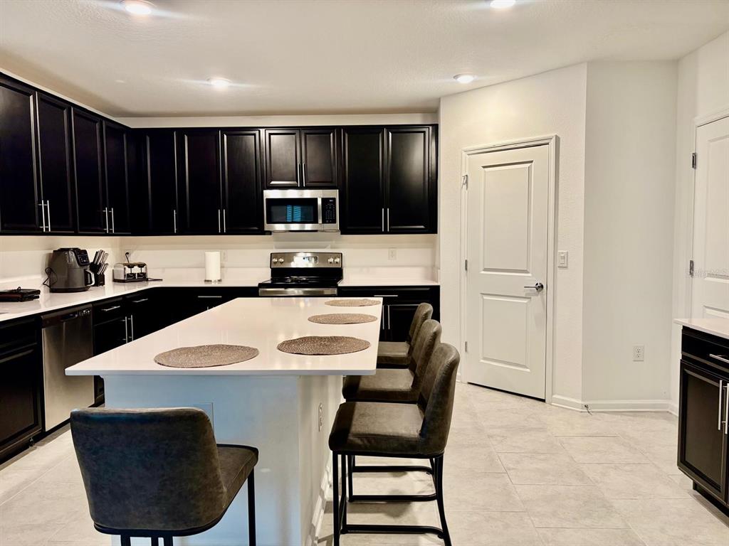 A kitchen features dark cabinets, white countertops, a central island with seating, and tile flooring — 4220 BULL STREET, ST CLOUD, FL