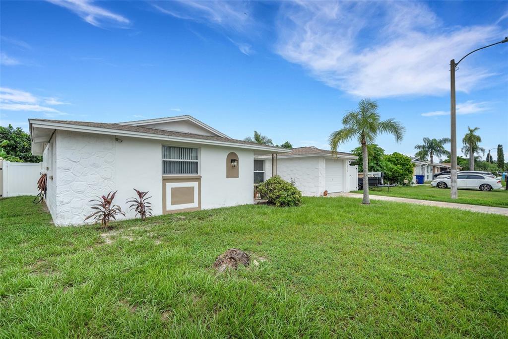 A white, single-story house with a stone-textured facade and an attached garage under a blue sky — 7234 OAKSHIRE DRIVE, PORT RICHEY, FL