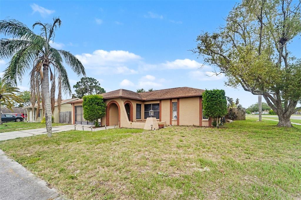 A single-story tan house with a brick-arched entryway and a palm tree in the yard — 1215 PERSIMMON DRIVE, HOLIDAY, FL