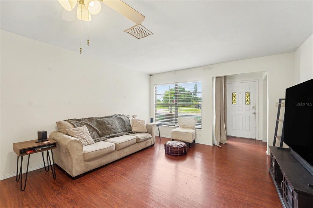 A living room features wood-look flooring, a beige sofa, a ceiling fan, and a front door — 1215 PERSIMMON DRIVE, HOLIDAY, FL