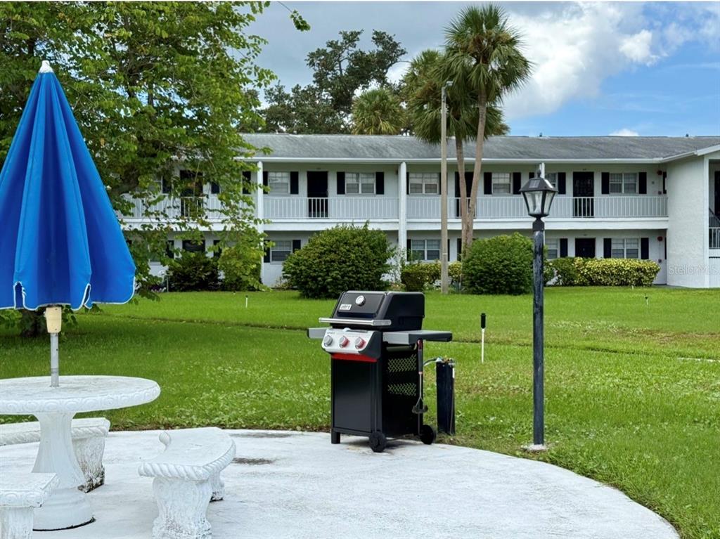 A patio with a grill, table, and blue umbrella sits before a two-story apartment building — 105 47TH AVENUE DRIVE W UNIT 374, BRADENTON, FL