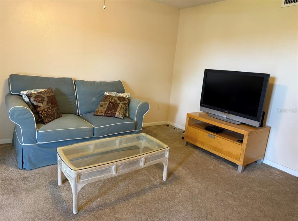 A living room features a blue sofa, a glass-topped coffee table, and a television stand — 105 47TH AVENUE DRIVE W UNIT 374, BRADENTON, FL