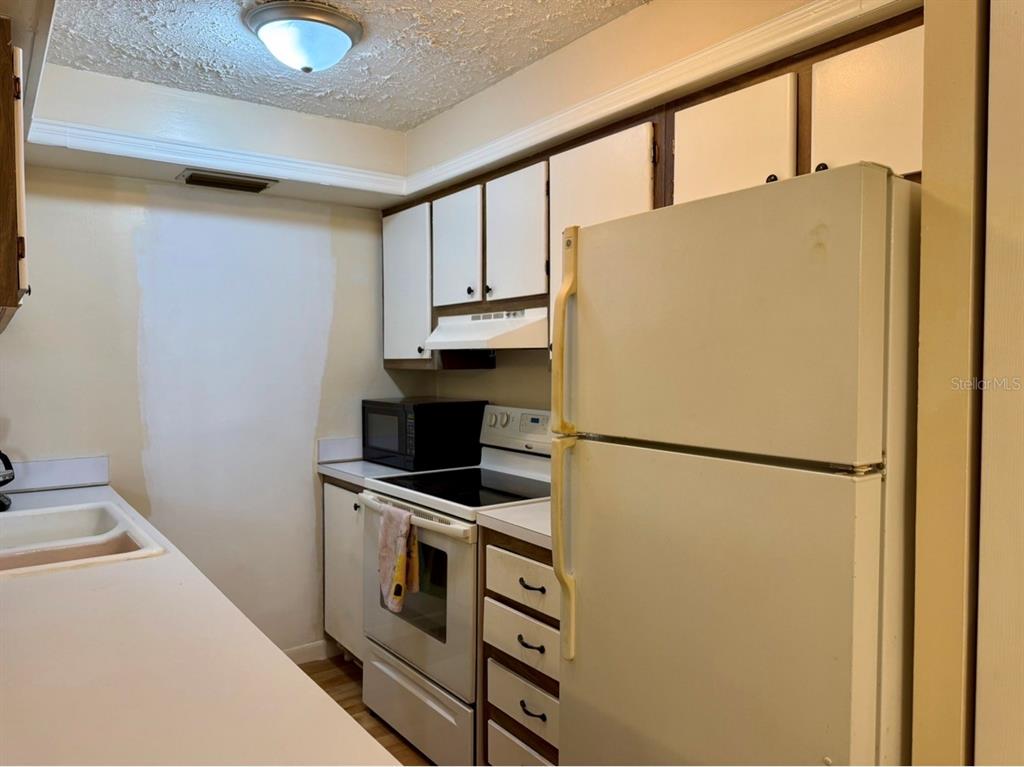 A galley-style kitchen features white cabinets, a white refrigerator, and a white electric range — 105 47TH AVENUE DRIVE W UNIT 374, BRADENTON, FL