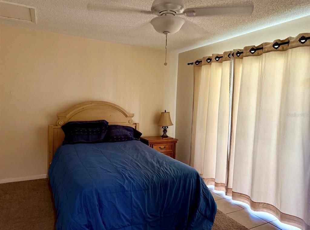A bedroom features a bed with a blue comforter, a nightstand, and floor-to-ceiling curtains — 105 47TH AVENUE DRIVE W UNIT 374, BRADENTON, FL