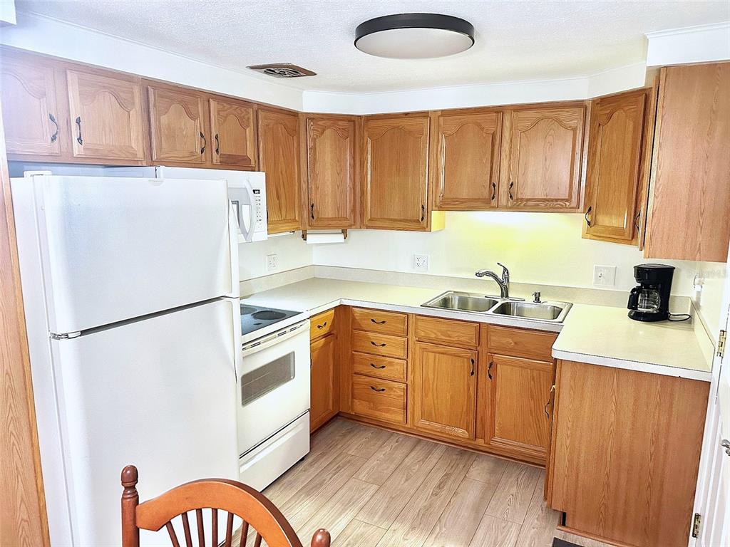 A kitchen features wood cabinets, white appliances, laminate countertops, and light wood-look flooring — 2000 E BAY DRIVE UNIT 83, LARGO, FL