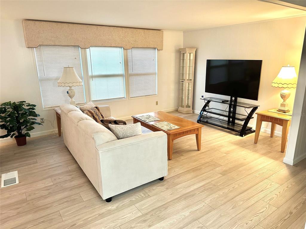A living room features light wood-look flooring, a beige sofa, a coffee table, and a television — 2000 E BAY DRIVE UNIT 83, LARGO, FL