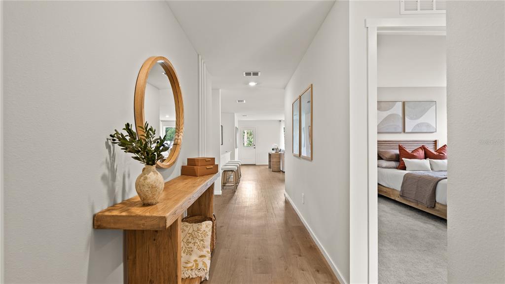 A hallway with a wooden console table, round mirror, and an adjacent bedroom entrance — 6113 SWAMP BAY DRIVE, EDGEWATER, FL