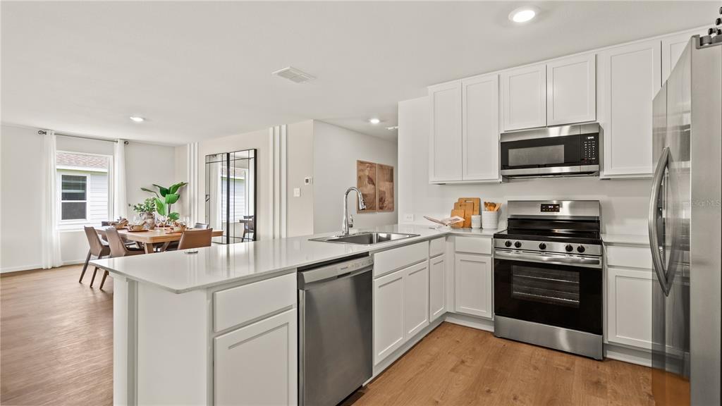 A modern kitchen with white cabinets, stainless steel appliances, and a quartz island countertop — 6113 SWAMP BAY DRIVE, EDGEWATER, FL