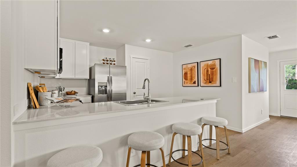 A modern kitchen features white cabinets, stainless steel appliances, a quartz island, and bar seating — 6113 SWAMP BAY DRIVE, EDGEWATER, FL