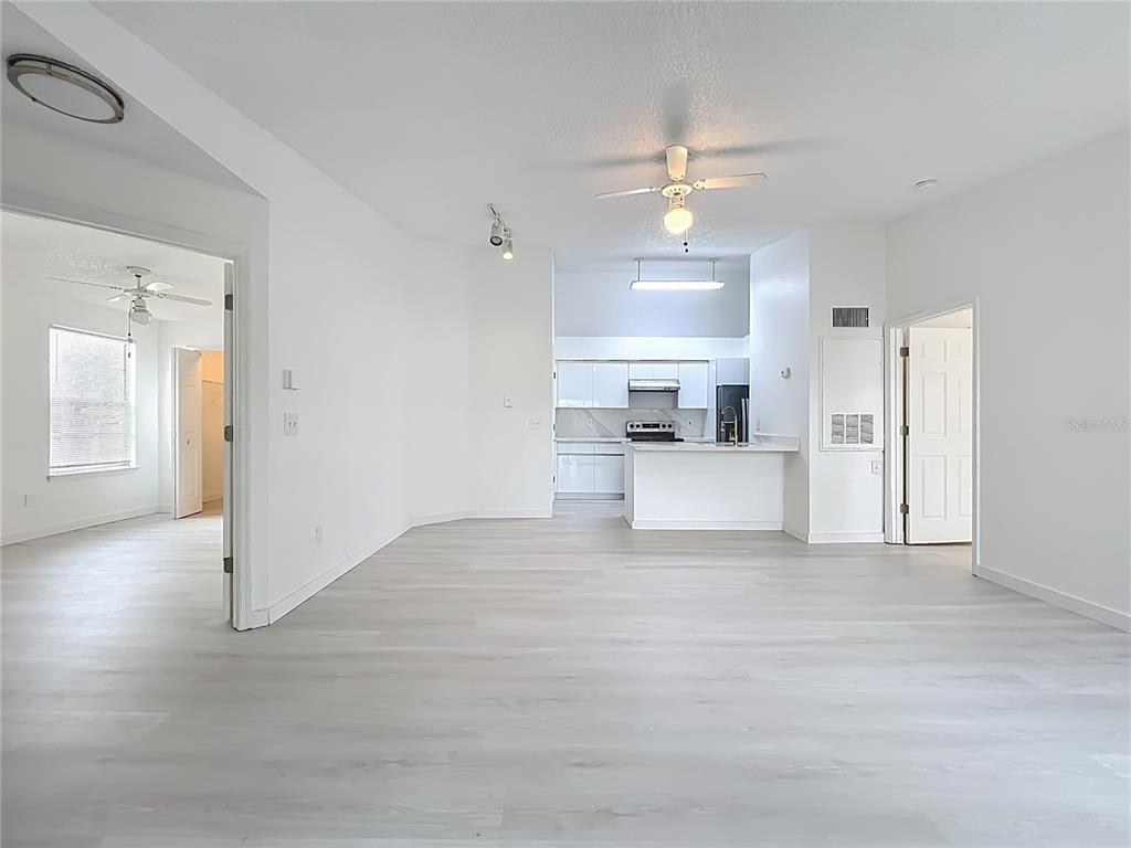 An open-concept living area with light wood-look flooring leads to a white kitchen — 2225 METROPOLITAN WAY UNIT 1225, ORLANDO, FL