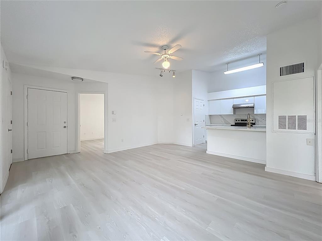 An open-concept living area features light wood-look flooring, white walls, and a kitchen with white cabinetry — 2225 METROPOLITAN WAY UNIT 1225, ORLANDO, FL