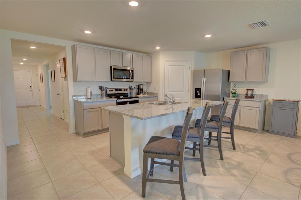 A kitchen with light gray cabinets, granite countertops, a central island, and three bar stools — 35712 DOVELAND DRIVE, ZEPHYRHILLS, FL