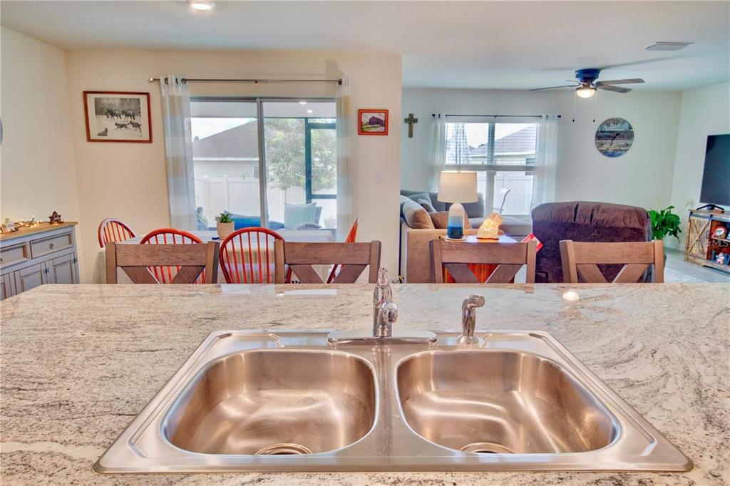 A kitchen island with a double stainless steel sink overlooks a dining and living area — 35712 DOVELAND DRIVE, ZEPHYRHILLS, FL