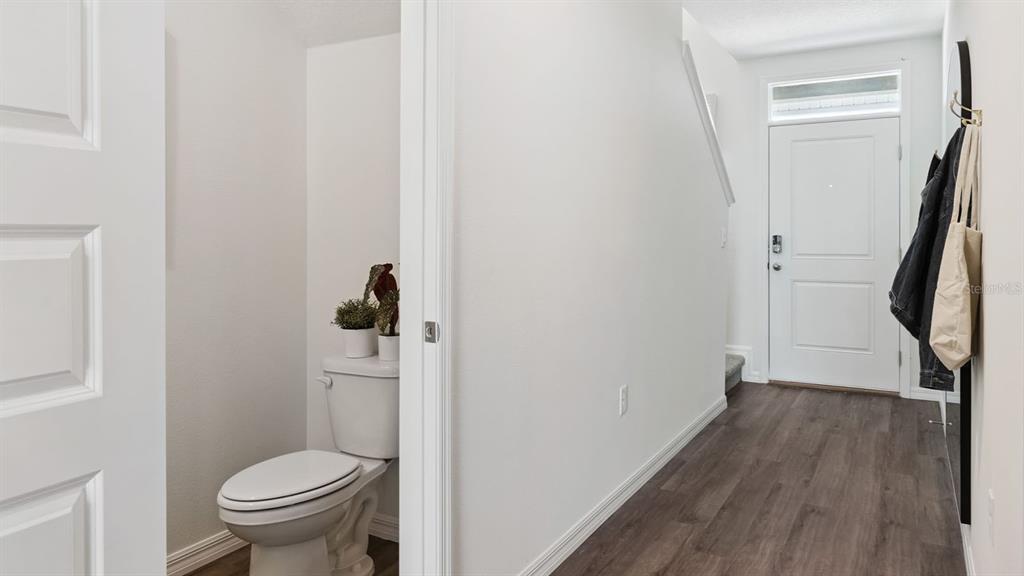 A hallway with wood-look flooring leads to a front door and a small powder room — 4294 BUTTERSCOTCH CIRCLE, LAKELAND, FL