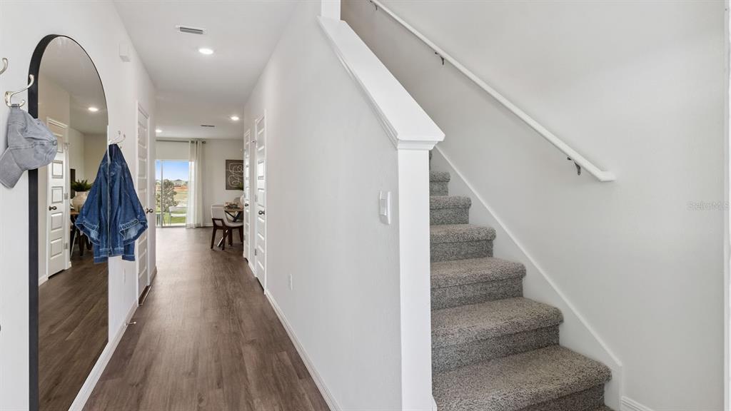 A hallway with wood-look flooring leads to a dining area, with carpeted stairs on the right — 4294 BUTTERSCOTCH CIRCLE, LAKELAND, FL