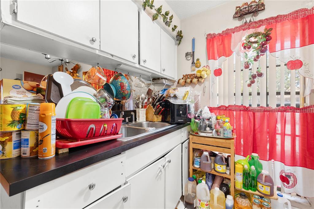 A kitchen features white cabinets, a black countertop, a stainless steel sink, and red curtains — 4200 37TH STREET S, ST PETERSBURG, FL