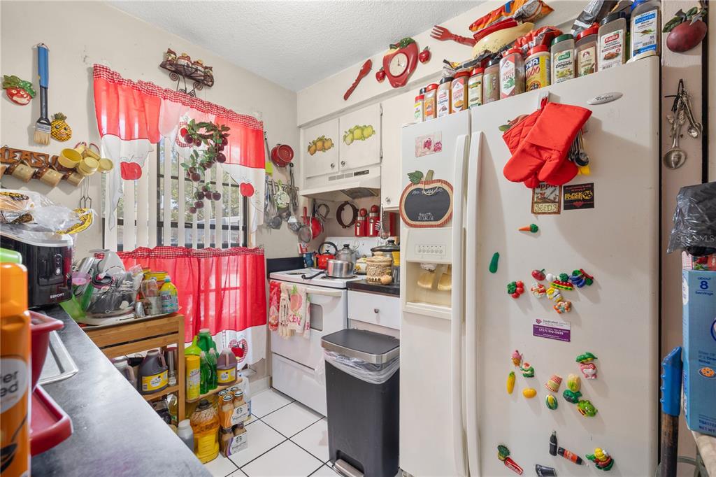 A kitchen features white appliances, tiled flooring, and numerous decorative magnets on the refrigerator — 4200 37TH STREET S, ST PETERSBURG, FL