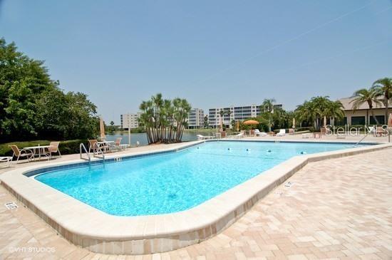 A multi-story apartment building stands behind a low clubhouse and pool overlooking a large lake — 9950 62ND TERRACE N UNIT 112, ST PETERSBURG, FL