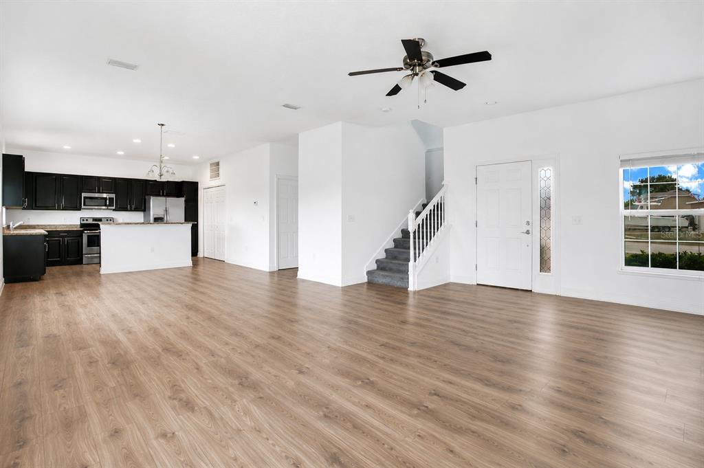 An open-concept living area features wood-look flooring, a kitchen with dark cabinets, and a staircase — 1370 SALISBURY DRIVE, WINTER HAVEN, FL