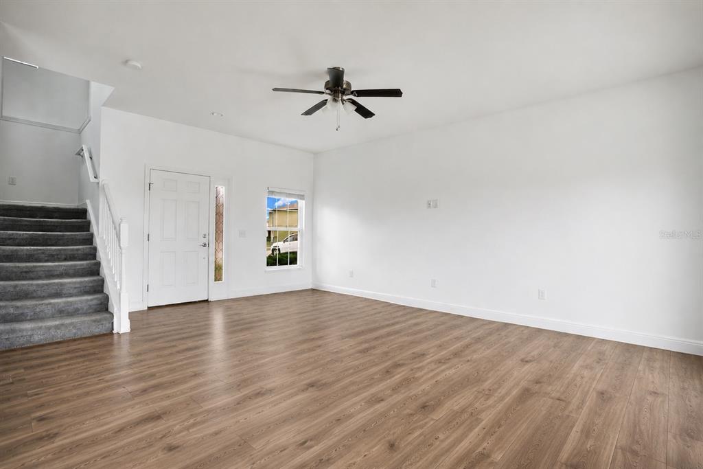 An empty living room features wood-look flooring, white walls, a ceiling fan, and carpeted stairs — 1370 SALISBURY DRIVE, WINTER HAVEN, FL