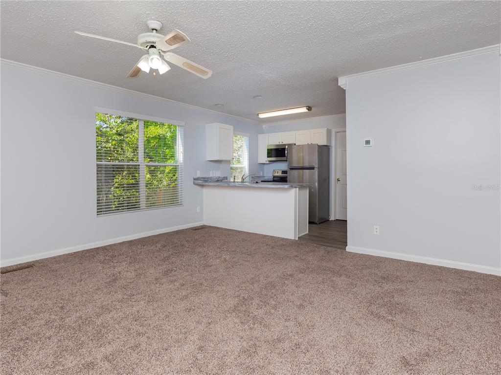 A living room with carpeted flooring opens to a kitchen featuring stainless steel appliances — 2905 SW ARCHER ROAD UNIT 4001, GAINESVILLE, FL