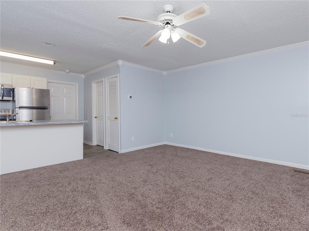 A carpeted living room features a ceiling fan and an adjacent kitchen with stainless appliances — 2905 SW ARCHER ROAD UNIT 4001, GAINESVILLE, FL
