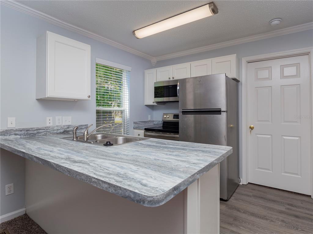 A kitchen features a marble-patterned countertop, stainless steel appliances, and white cabinetry — 2905 SW ARCHER ROAD UNIT 4001, GAINESVILLE, FL