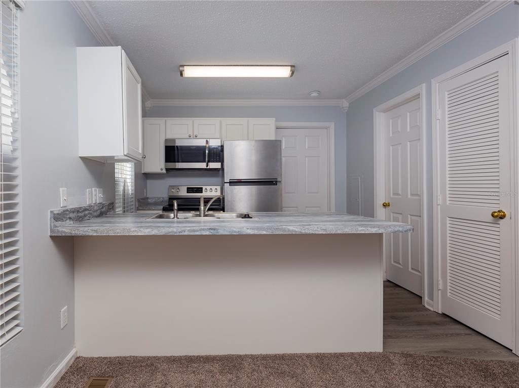 A kitchen features a breakfast bar, stainless steel appliances, white cabinets, and gray countertops — 2905 SW ARCHER ROAD UNIT 4001, GAINESVILLE, FL